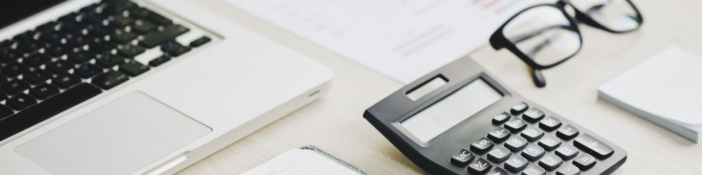 View of a desk with calculator, glasses, documents and laptop.